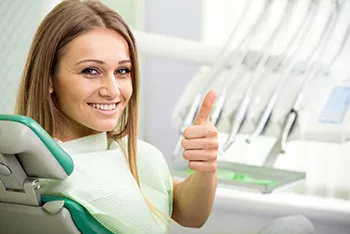 young woman sitting in dental chair giving thumb's up